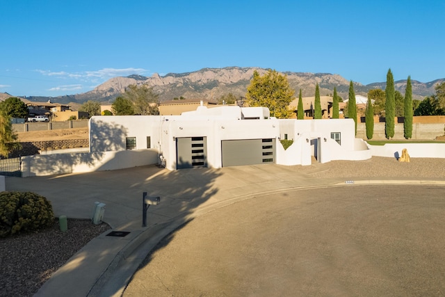 pueblo-style house with an attached garage, fence, a mountain view, and stucco siding