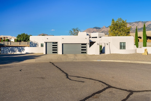 pueblo-style home with a garage, fence, a mountain view, and stucco siding