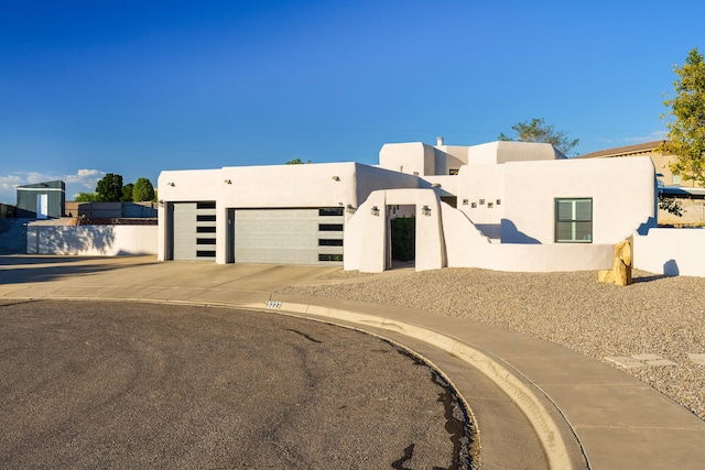 pueblo revival-style home featuring driveway, an attached garage, and stucco siding