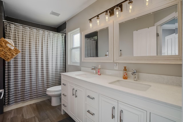 full bathroom with toilet, double vanity, visible vents, and a sink