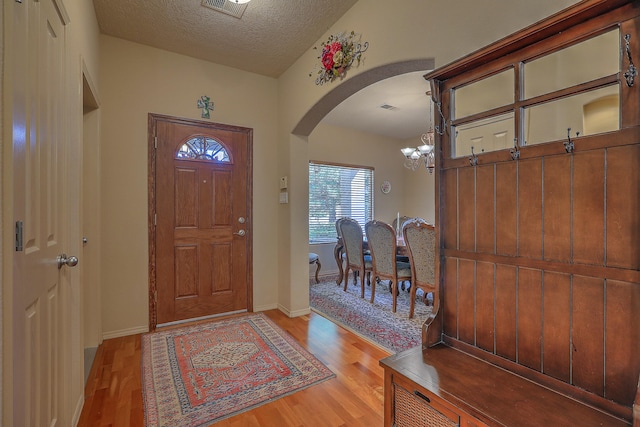 entryway featuring a textured ceiling, wood-type flooring, vaulted ceiling, and a chandelier