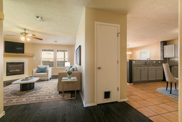 living room with ceiling fan, a textured ceiling, light hardwood / wood-style flooring, and sink