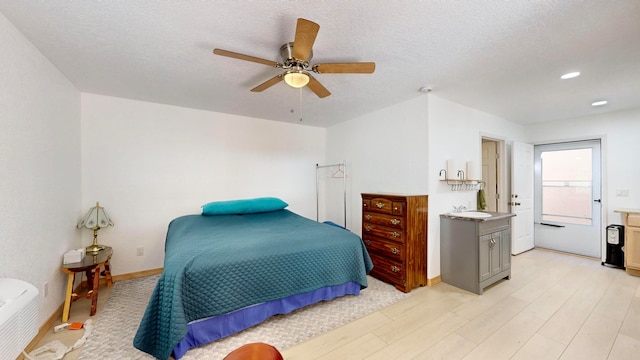 bedroom with light wood-type flooring, ensuite bath, ceiling fan, and a textured ceiling