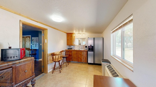 kitchen with light tile patterned flooring, a textured ceiling, crown molding, sink, and stainless steel fridge with ice dispenser