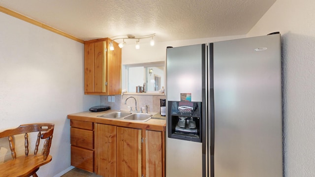 kitchen featuring decorative backsplash, a textured ceiling, stainless steel refrigerator with ice dispenser, ornamental molding, and sink