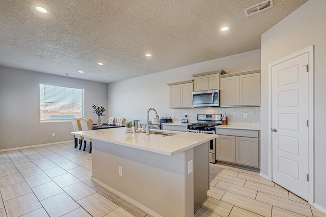 kitchen featuring a kitchen island with sink, sink, appliances with stainless steel finishes, gray cabinets, and a textured ceiling