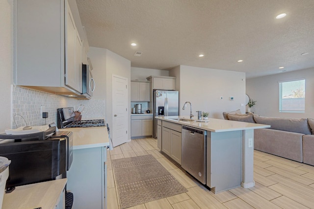 kitchen featuring light wood-type flooring, sink, stainless steel appliances, an island with sink, and a textured ceiling