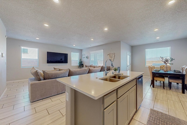 kitchen with dishwasher, a kitchen island with sink, sink, and a textured ceiling