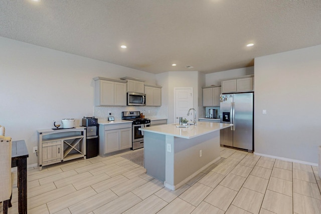 kitchen with appliances with stainless steel finishes, gray cabinetry, sink, and a center island with sink