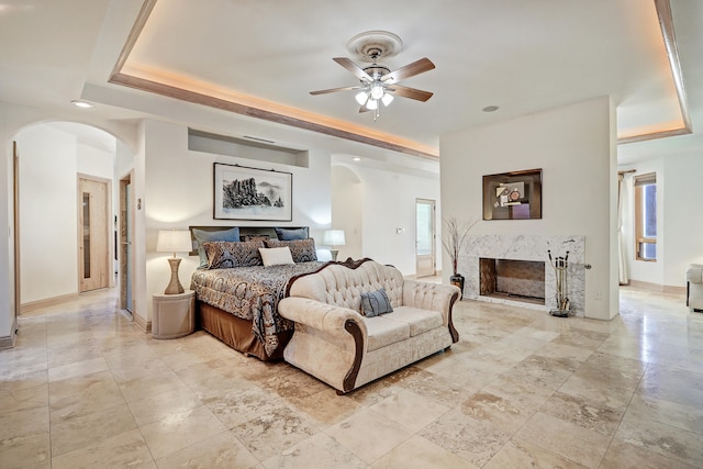 bedroom with a raised ceiling, ceiling fan, and a premium fireplace