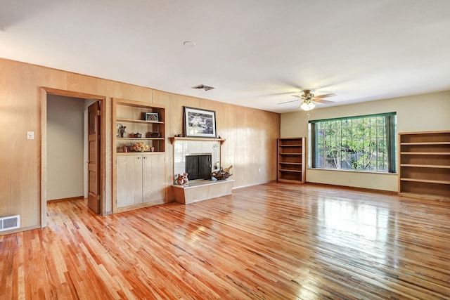 unfurnished living room featuring ceiling fan, wooden walls, light hardwood / wood-style floors, and built in shelves