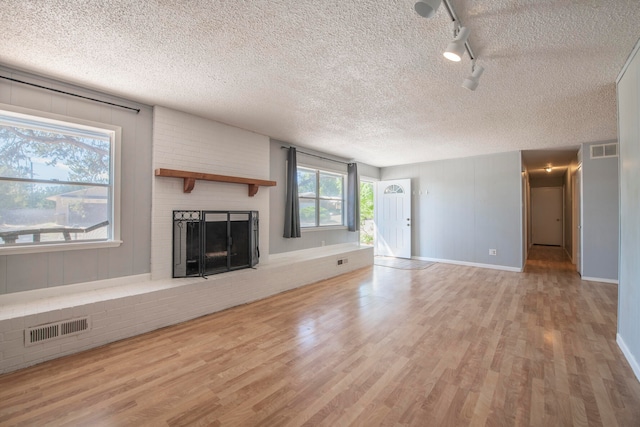 unfurnished living room with light wood-type flooring, a textured ceiling, and a brick fireplace