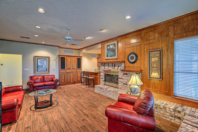 living room featuring ceiling fan, wood-type flooring, a fireplace, ornamental molding, and a textured ceiling