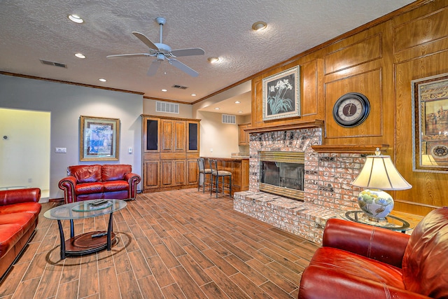 living room featuring ornamental molding, hardwood / wood-style flooring, a brick fireplace, and a textured ceiling