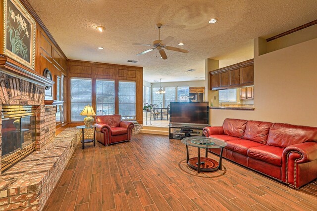 living room featuring wood walls, ceiling fan with notable chandelier, crown molding, hardwood / wood-style floors, and a textured ceiling