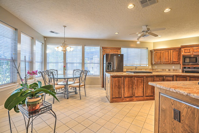 kitchen featuring ceiling fan with notable chandelier, hanging light fixtures, appliances with stainless steel finishes, and a textured ceiling