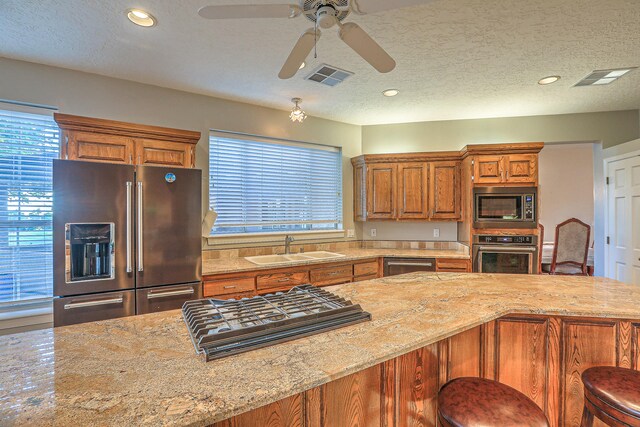 kitchen featuring ceiling fan, sink, a textured ceiling, stainless steel appliances, and a kitchen bar