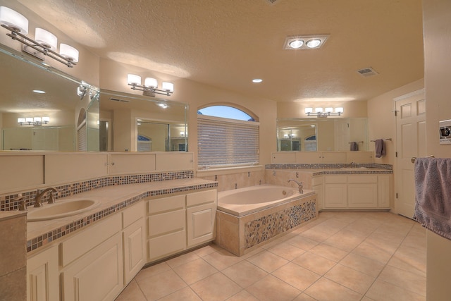 bathroom with a textured ceiling, tile patterned floors, vanity, and tiled bath