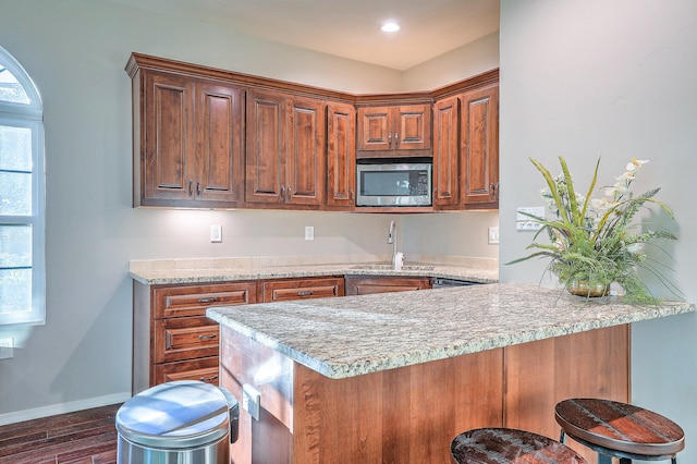 kitchen featuring dark hardwood / wood-style flooring, stainless steel microwave, sink, kitchen peninsula, and a kitchen bar