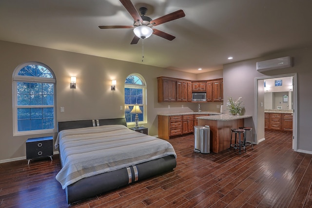 bedroom with an AC wall unit, ensuite bath, ceiling fan, and dark hardwood / wood-style flooring