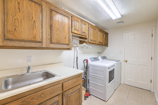 laundry area with light tile patterned floors, sink, a textured ceiling, washer and clothes dryer, and cabinets