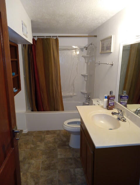 full bathroom featuring shower / bath combo, a textured ceiling, vanity, and toilet