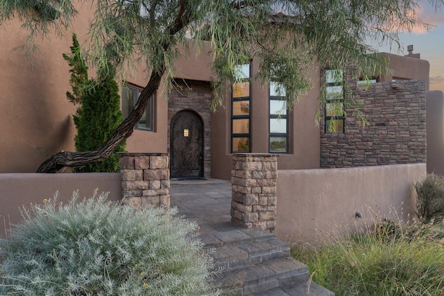 exterior space with stone siding, fence, and stucco siding