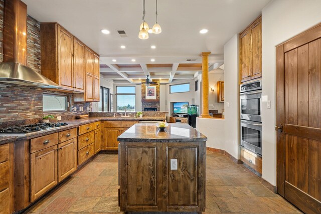 kitchen with appliances with stainless steel finishes, a center island, wall chimney range hood, sink, and hanging light fixtures