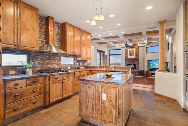 kitchen featuring wall chimney exhaust hood, a kitchen island, open floor plan, decorative light fixtures, and stainless steel gas cooktop