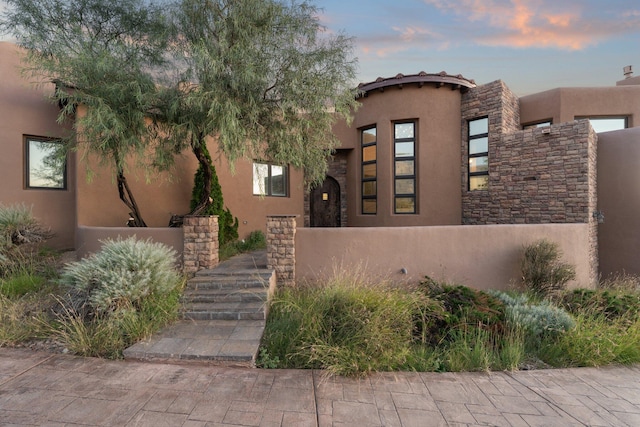 view of front facade featuring stone siding, a fenced front yard, and stucco siding