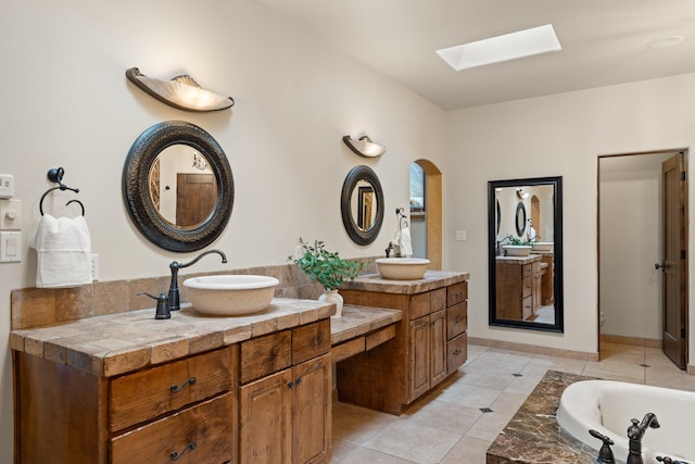 full bath with a tub to relax in, a skylight, vanity, and tile patterned floors