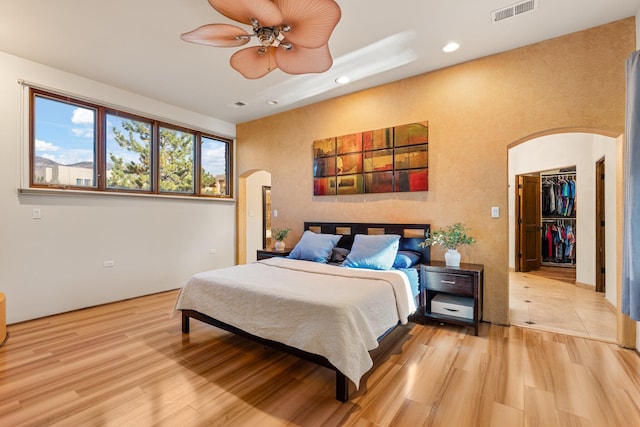 bedroom with arched walkways, recessed lighting, visible vents, light wood finished floors, and a walk in closet