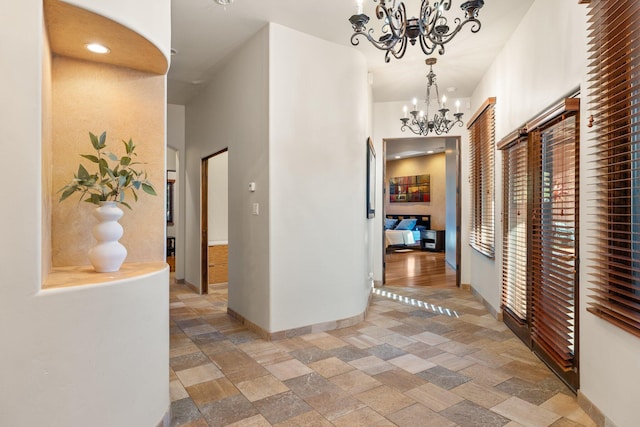 corridor featuring baseboards, a chandelier, and stone tile flooring