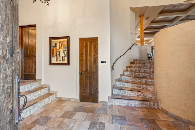 interior space with a high ceiling, beamed ceiling, stone tile flooring, and baseboards