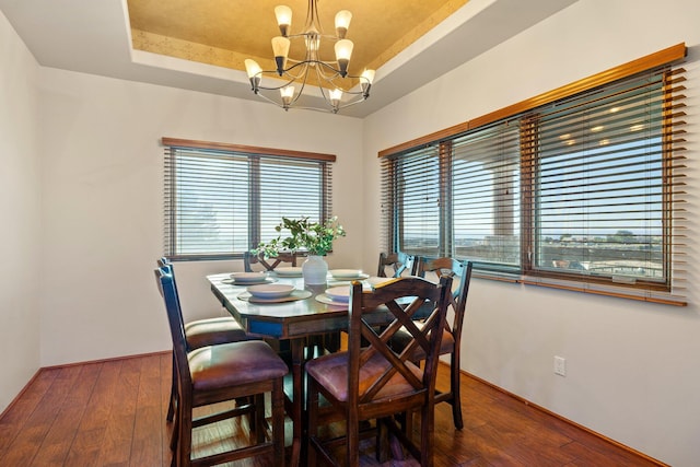 dining area featuring dark wood-type flooring, a tray ceiling, and a chandelier