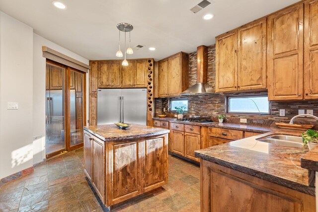 kitchen featuring pendant lighting, stainless steel appliances, a sink, a kitchen island, and wall chimney exhaust hood