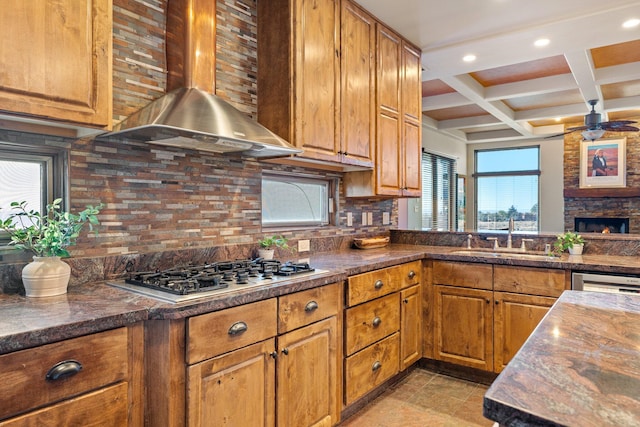 kitchen with coffered ceiling, wall chimney exhaust hood, appliances with stainless steel finishes, backsplash, and a sink