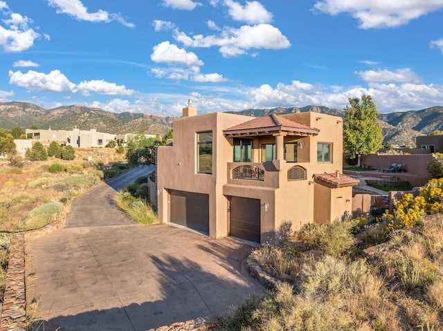 pueblo revival-style home featuring a garage, a mountain view, a balcony, and stucco siding