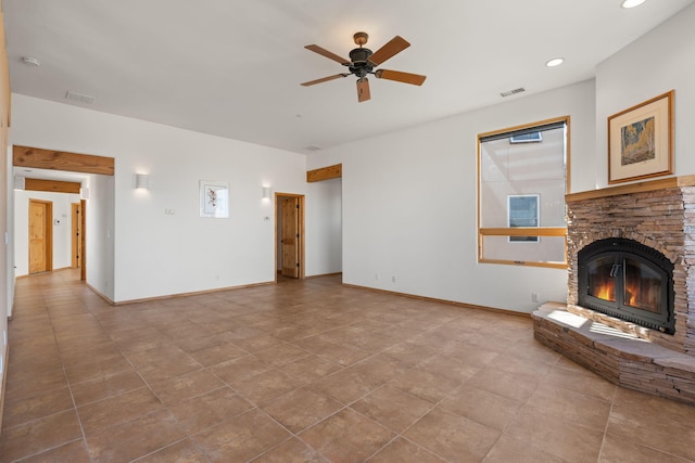 unfurnished living room featuring a wealth of natural light, ceiling fan, light tile patterned flooring, and a stone fireplace