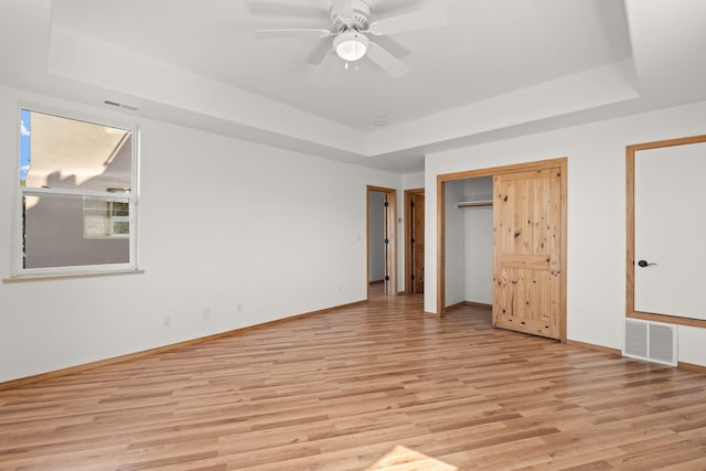 unfurnished bedroom featuring light wood-type flooring, ceiling fan, and a raised ceiling