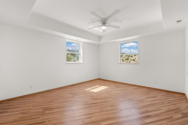 unfurnished room with a raised ceiling, ceiling fan, and light hardwood / wood-style flooring