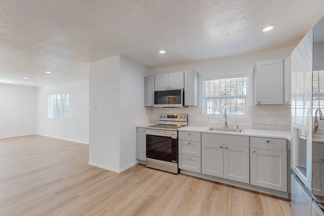 kitchen with light wood-type flooring, a textured ceiling, sink, backsplash, and appliances with stainless steel finishes