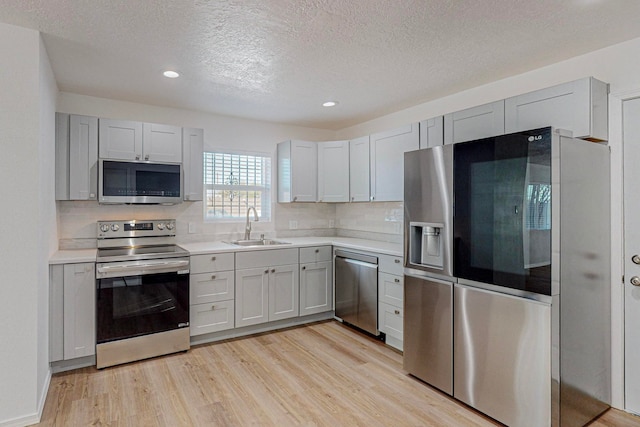 kitchen with sink, a textured ceiling, light hardwood / wood-style flooring, backsplash, and stainless steel appliances