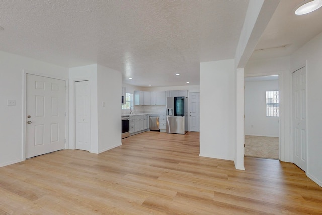 unfurnished living room featuring light wood-type flooring, sink, and a healthy amount of sunlight