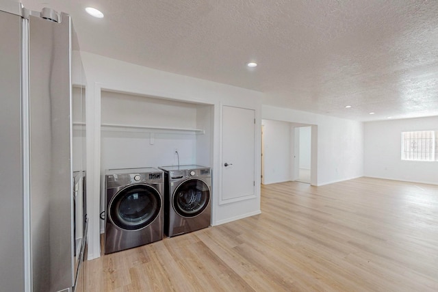 washroom with a textured ceiling, light wood-type flooring, and independent washer and dryer