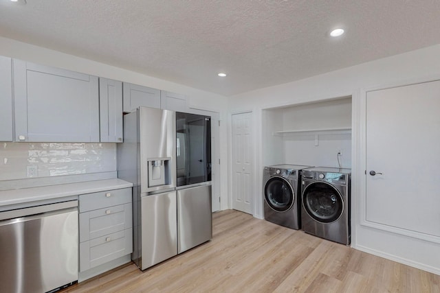 kitchen with a textured ceiling, tasteful backsplash, light hardwood / wood-style flooring, appliances with stainless steel finishes, and washer and clothes dryer