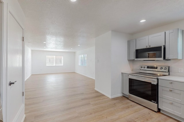 kitchen with gray cabinets, appliances with stainless steel finishes, light wood-type flooring, and a textured ceiling