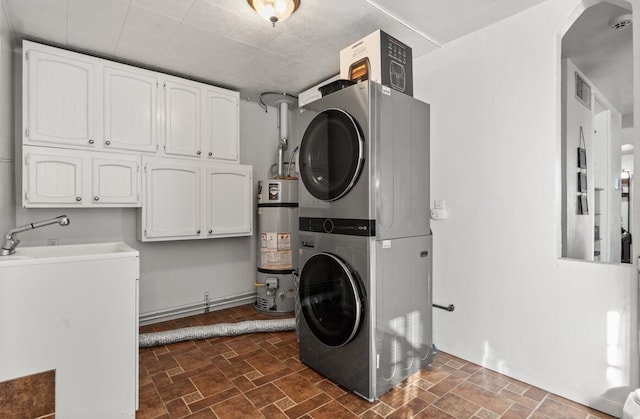 laundry area with stacked washer and clothes dryer, secured water heater, and cabinets