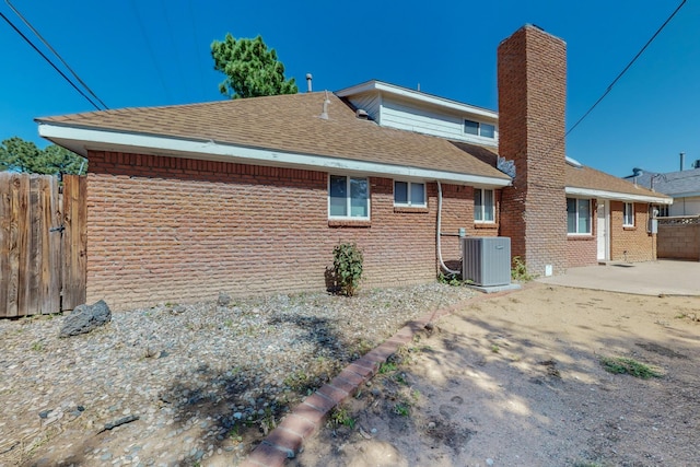 back of property featuring a patio, central AC unit, brick siding, fence, and roof with shingles