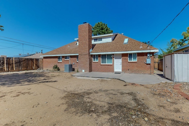 rear view of property featuring central air condition unit, fence, a storage unit, and brick siding